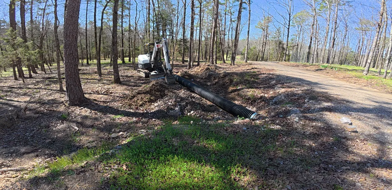 Culvert pipe laid in a trench beside a gravel road, mini-excavator behind it