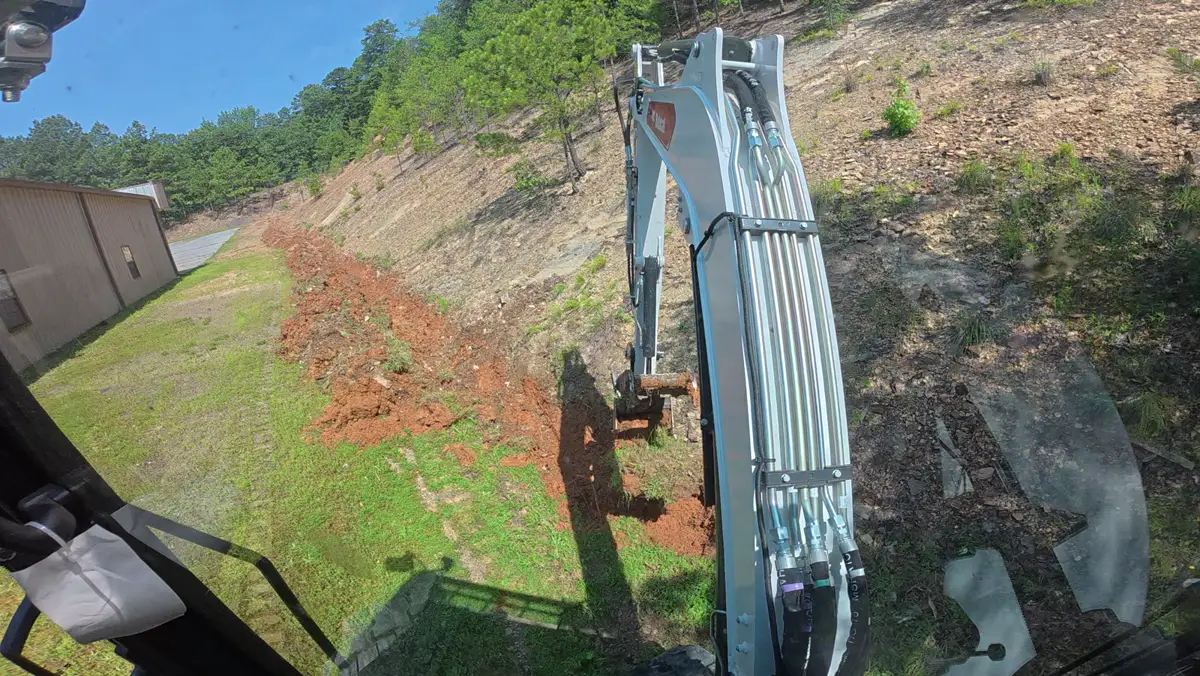 Mini-excavator cutting a drainage ditch along a slope