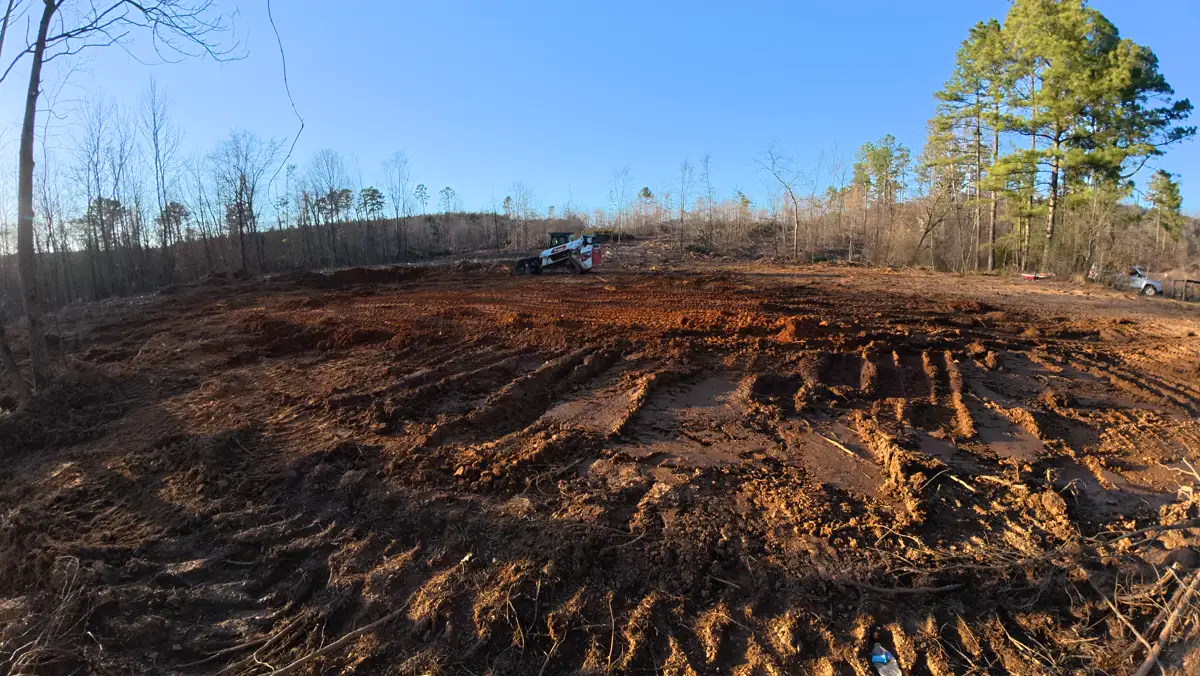 Compact track loader shaping exposed ground at a cleared site